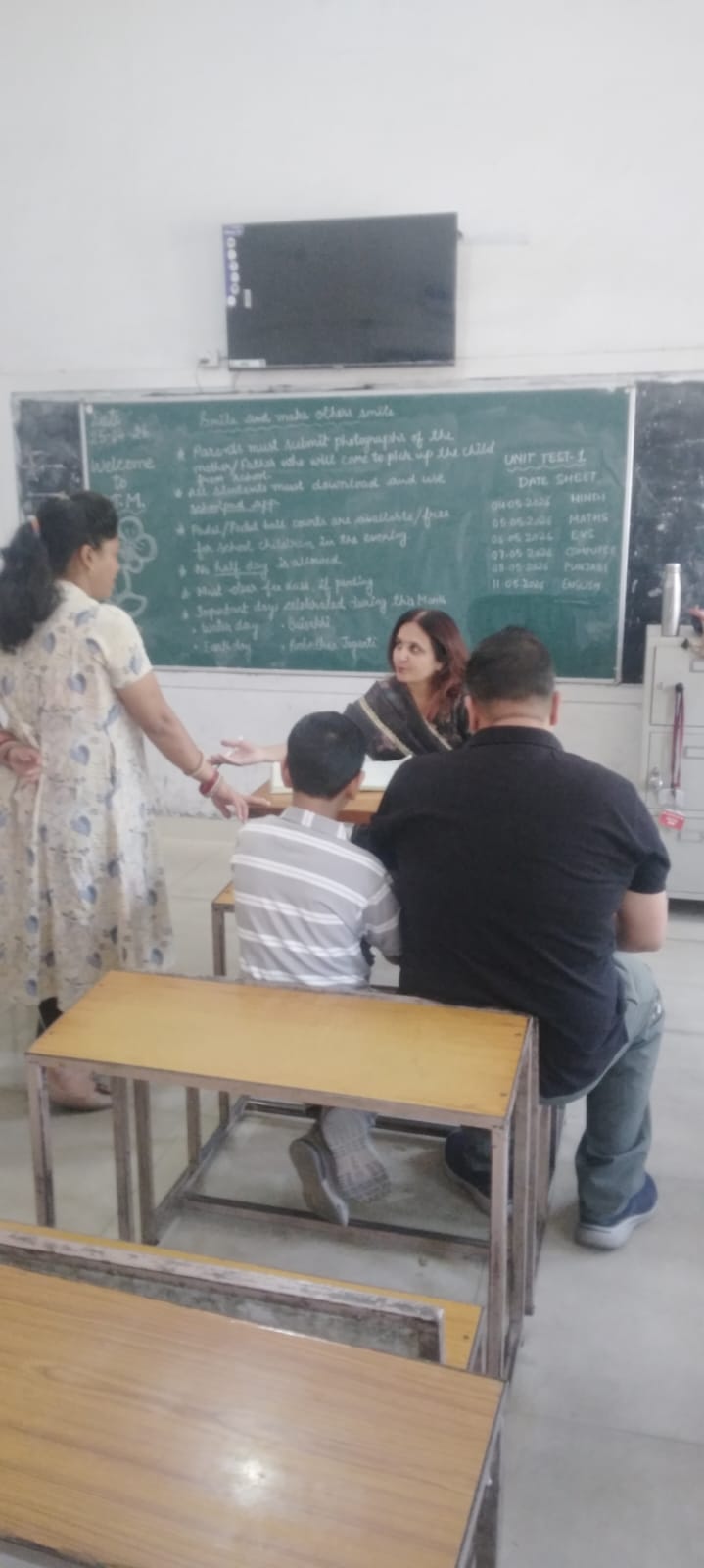 Teacher at desk with unit test date sheet on blackboard